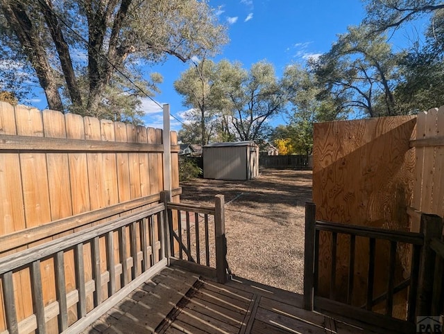 wooden deck featuring a fenced backyard, a storage unit, and an outbuilding