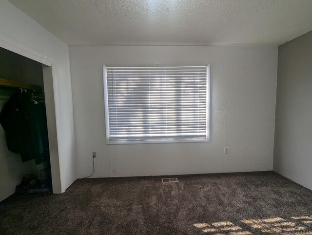 empty room with visible vents, dark carpet, and a textured ceiling