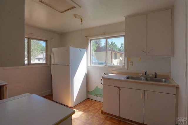 kitchen with light countertops, freestanding refrigerator, white cabinets, and a sink