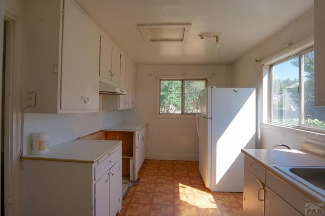 kitchen featuring under cabinet range hood, light countertops, freestanding refrigerator, and white cabinets