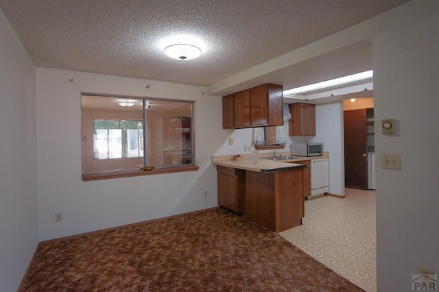 kitchen featuring brown cabinetry, dishwasher, stainless steel microwave, a peninsula, and light countertops