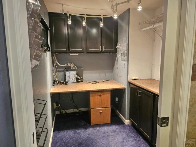 home office featuring dark colored carpet, built in study area, rail lighting, and baseboards