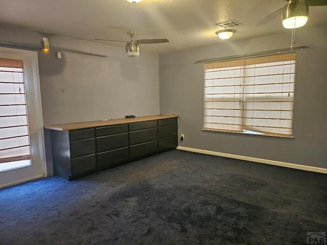 unfurnished bedroom featuring visible vents, dark carpet, a ceiling fan, a textured ceiling, and baseboards