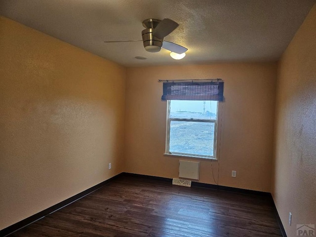 unfurnished room featuring a textured wall, dark wood-type flooring, visible vents, a ceiling fan, and baseboards