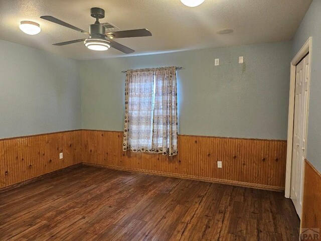 spare room featuring a wainscoted wall, wood walls, dark wood finished floors, and a textured ceiling