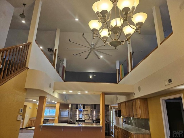 kitchen with brown cabinetry, a peninsula, light countertops, wall chimney range hood, and a chandelier