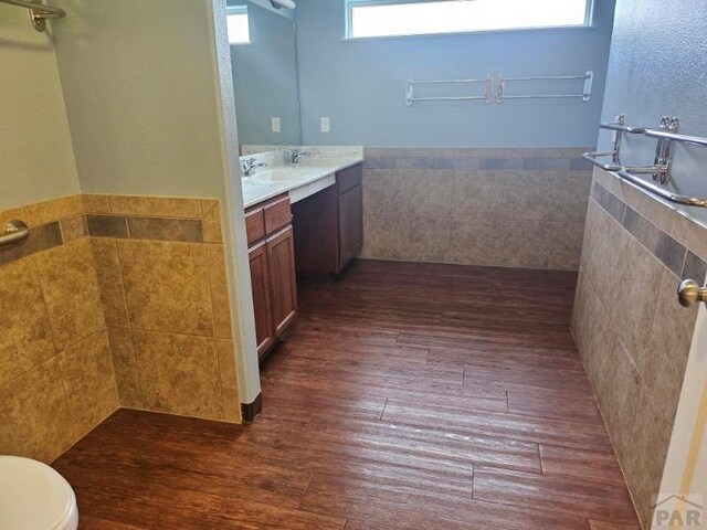 full bathroom featuring a wainscoted wall, tile walls, toilet, vanity, and wood finished floors