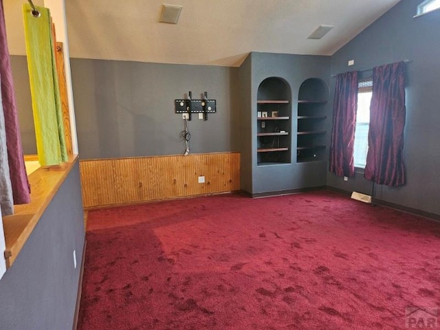 spare room with lofted ceiling, a wainscoted wall, carpet flooring, wood walls, and built in shelves