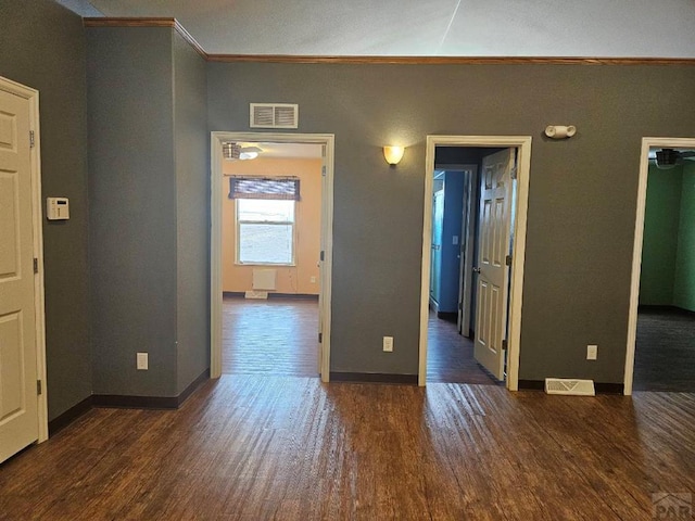 interior space featuring dark wood-style floors, visible vents, ornamental molding, and baseboards