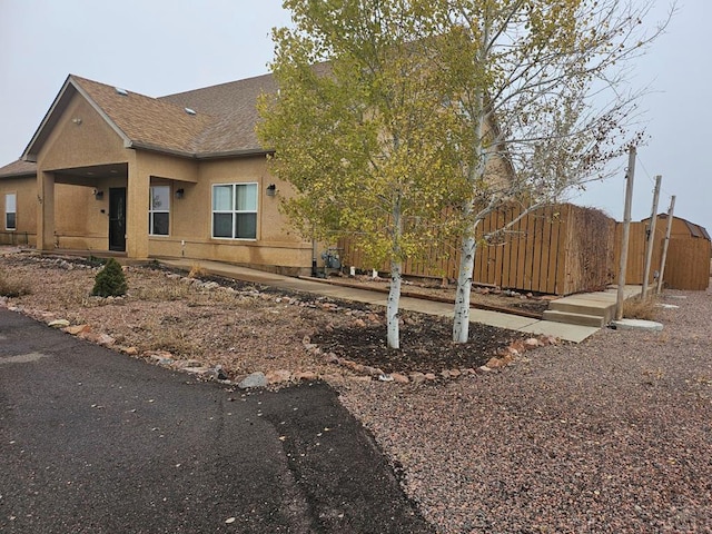 view of side of home featuring roof with shingles, fence, and stucco siding