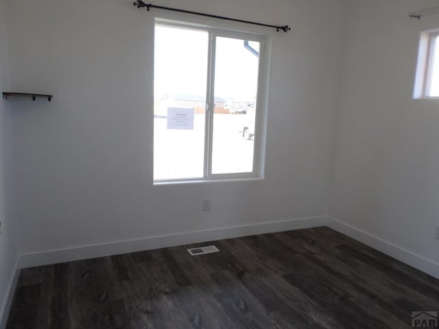 empty room featuring visible vents, baseboards, and dark wood-type flooring