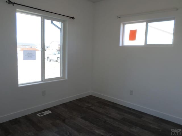 unfurnished room featuring dark wood-style floors, baseboards, and visible vents