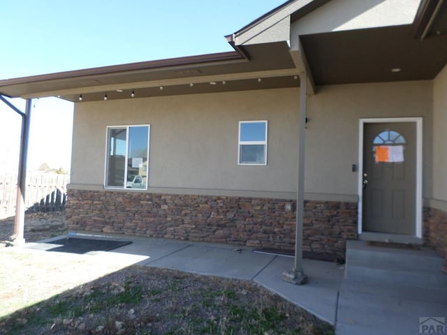 entrance to property with stucco siding, stone siding, and fence