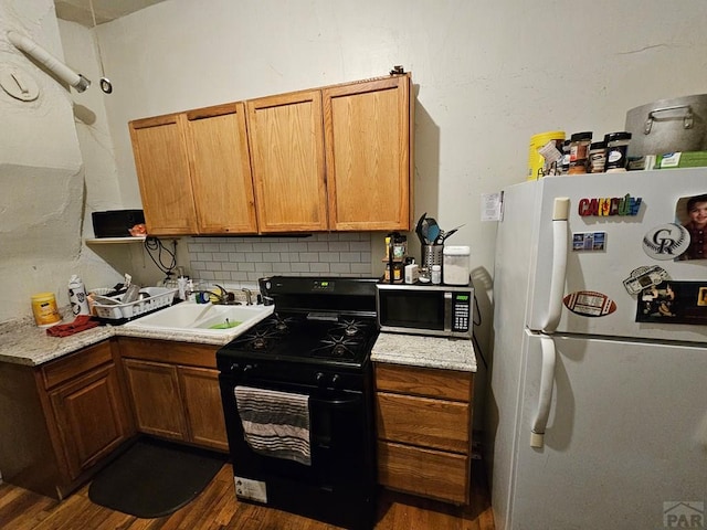 kitchen featuring stainless steel microwave, brown cabinets, freestanding refrigerator, a sink, and gas stove