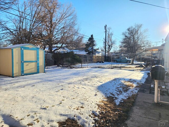 yard layered in snow featuring a fenced backyard, an outdoor structure, and a shed