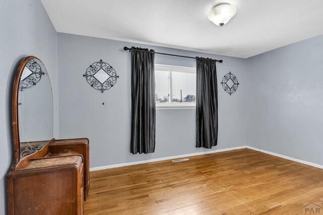 empty room featuring wood finished floors, visible vents, and baseboards