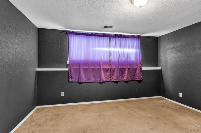 empty room with carpet floors, visible vents, and a textured wall