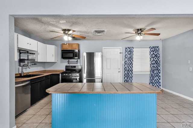 kitchen with tile counters, visible vents, appliances with stainless steel finishes, white cabinetry, and a sink