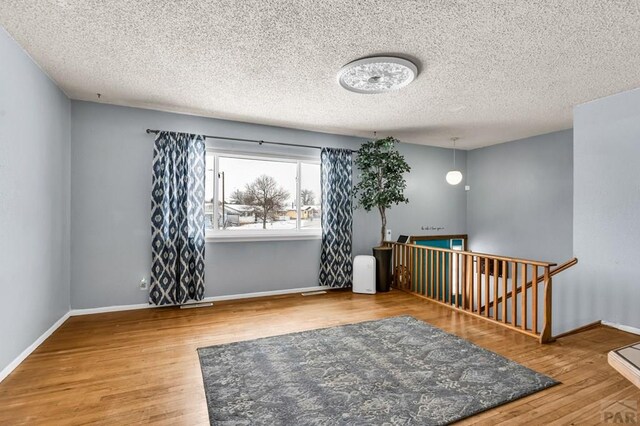 spare room with a textured ceiling, baseboards, and wood finished floors