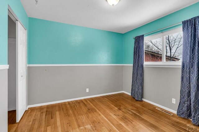 spare room with wood finished floors, visible vents, and baseboards