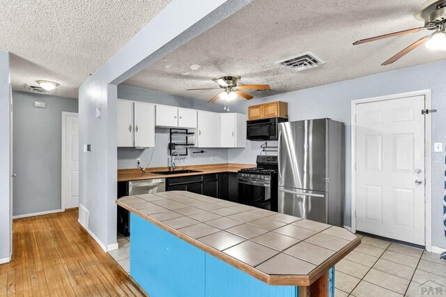 kitchen featuring visible vents, tile counters, white cabinets, stainless steel appliances, and a sink