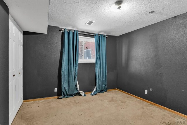 spare room featuring light carpet, baseboards, visible vents, a textured wall, and a textured ceiling