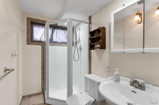 bathroom featuring toilet, a sink, baseboards, tile patterned floors, and a stall shower