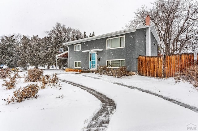 split foyer home featuring fence, a chimney, and stucco siding