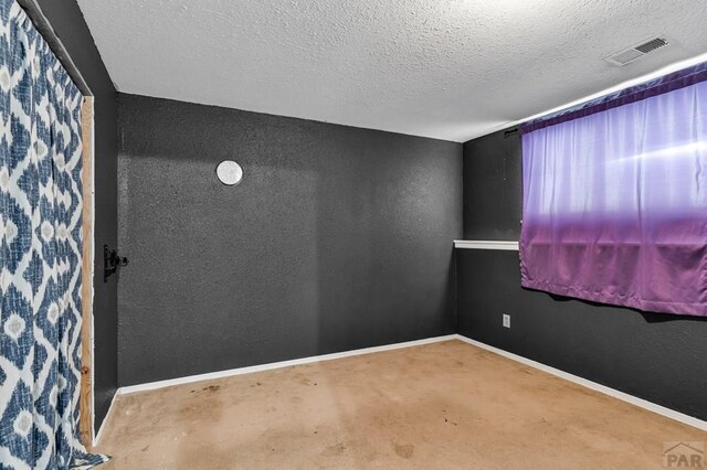 empty room featuring baseboards, visible vents, a textured ceiling, and a textured wall