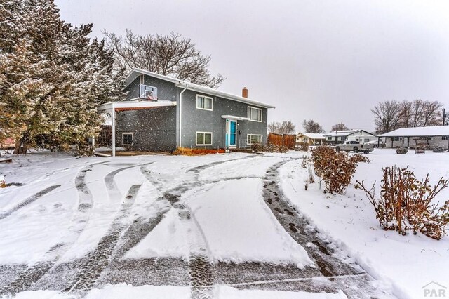 snow covered property featuring a chimney, fence, and stucco siding