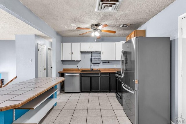 kitchen with stainless steel appliances, tile counters, visible vents, white cabinets, and a sink