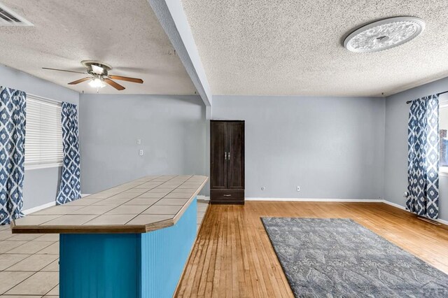 kitchen with ceiling fan, visible vents, baseboards, light wood-style floors, and tile counters