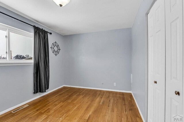 unfurnished bedroom with a closet, wood finished floors, visible vents, and baseboards