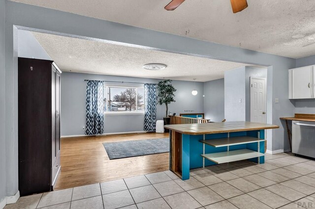 kitchen featuring tile countertops, light tile patterned floors, white cabinetry, open floor plan, and stainless steel dishwasher