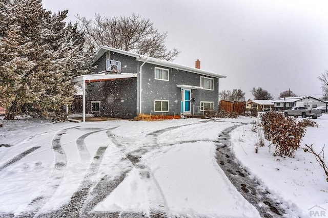 snow covered property featuring fence, a chimney, and stucco siding