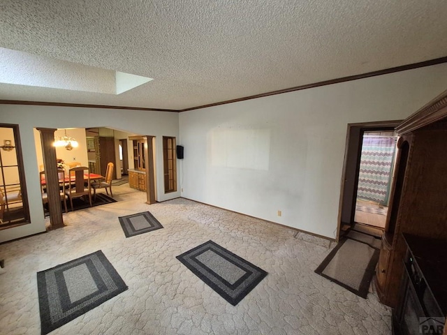 1106 10th St, Las Animas, CO 81054 - unfurnished living room featuring crown molding, light carpet, a textured ceiling, a chandelier, and decorative columns