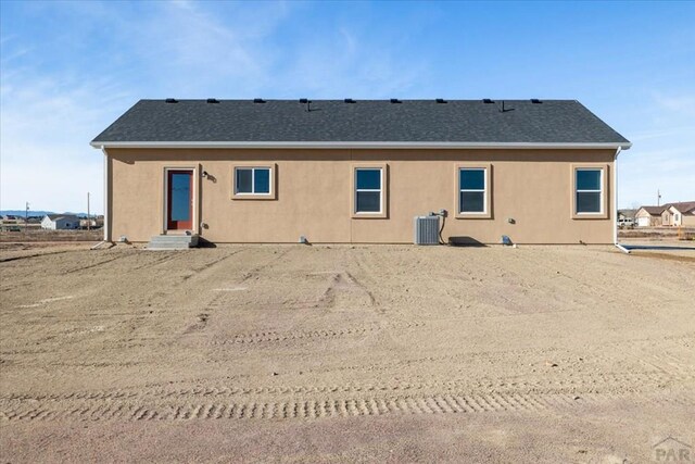 back of house featuring entry steps, stucco siding, roof with shingles, and central air condition unit