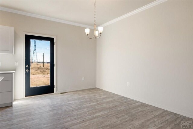 unfurnished room with a chandelier, ornamental molding, and wood finished floors