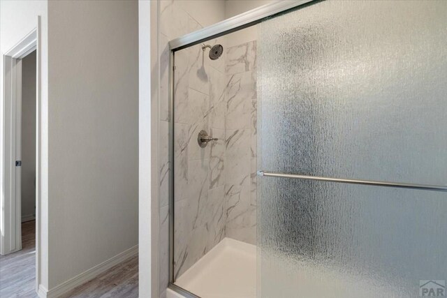 bathroom featuring wood finished floors, a shower stall, and baseboards