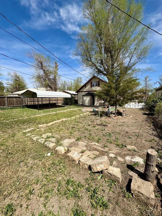 view of yard featuring a garage, an outbuilding, a carport, and fence