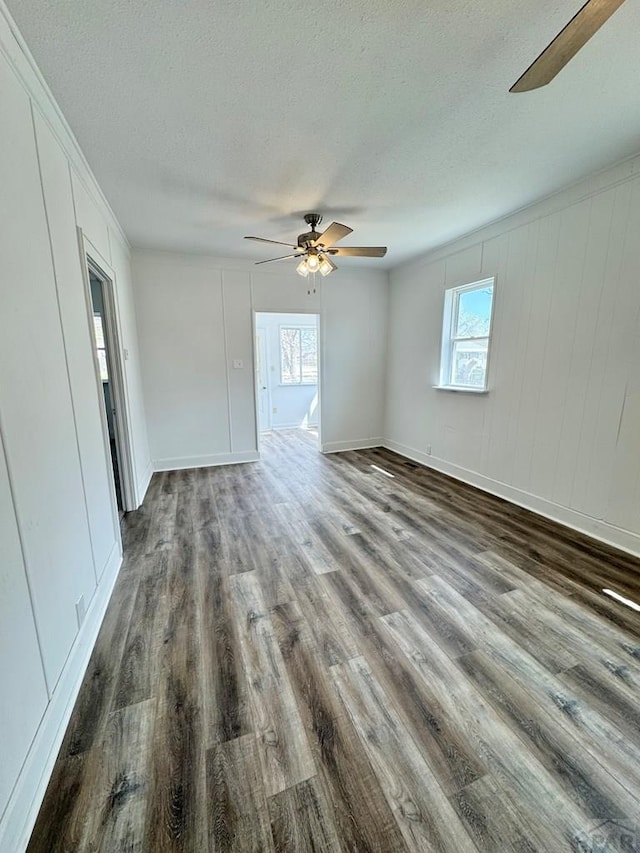 empty room featuring a textured ceiling, a ceiling fan, dark wood-style flooring, and a healthy amount of sunlight