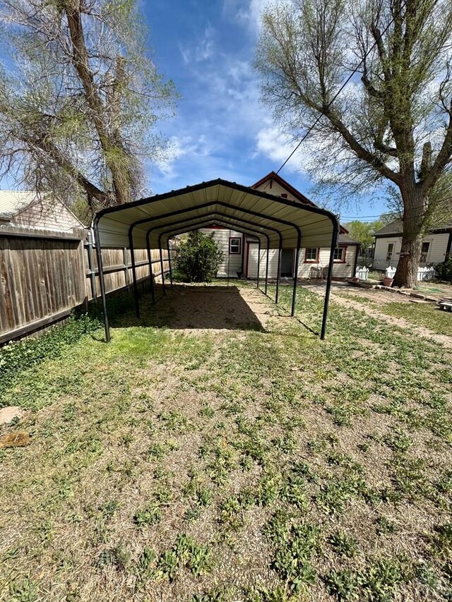 view of vehicle parking with fence, driveway, and a detached carport