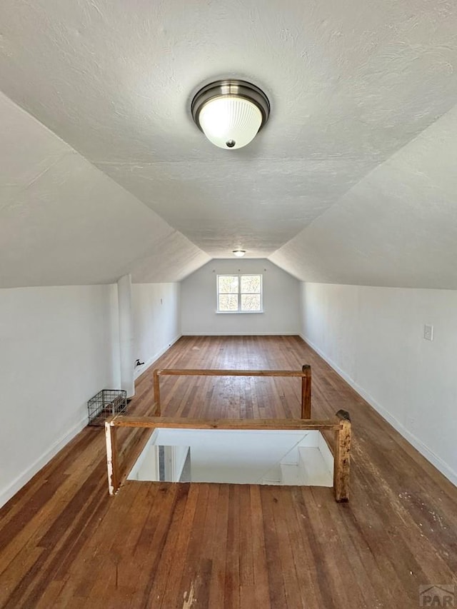 additional living space with wood-type flooring, lofted ceiling, a textured ceiling, and baseboards