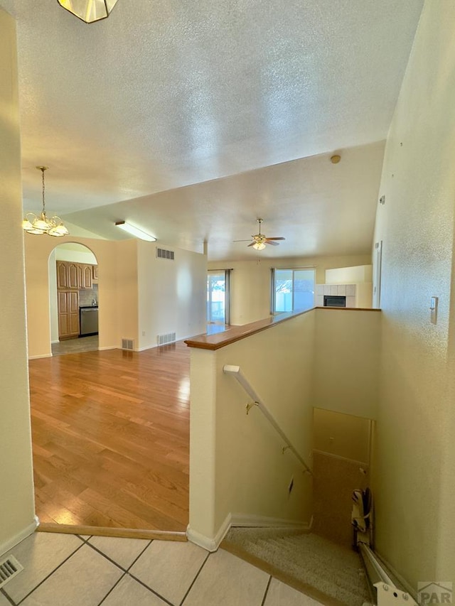 stairway with arched walkways, visible vents, a textured ceiling, and wood finished floors