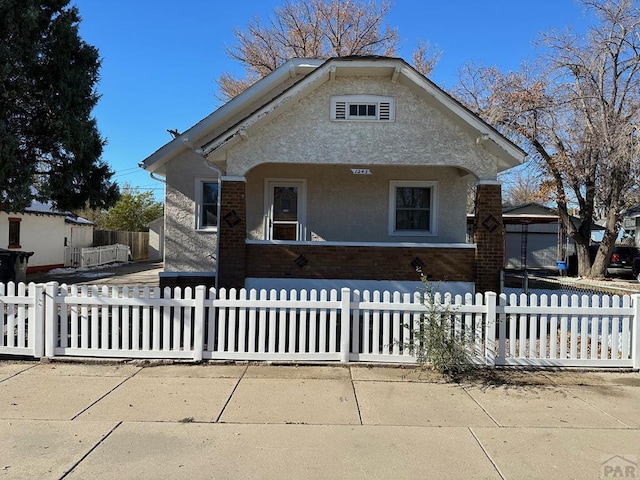 bungalow-style home featuring brick siding, a fenced front yard, and stucco siding