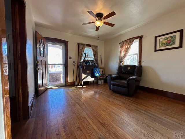 living area with ceiling fan, dark wood finished floors, a wealth of natural light, and baseboards