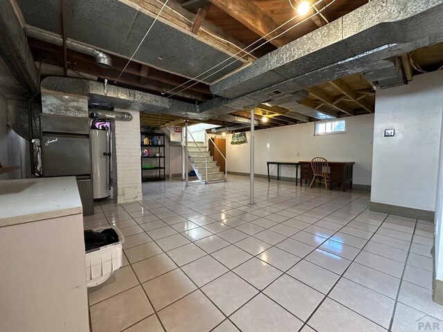 below grade area with stairs, fridge, baseboards, and tile patterned floors