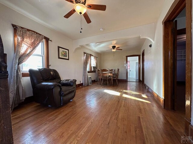 living area with a ceiling fan, arched walkways, dark wood finished floors, and baseboards