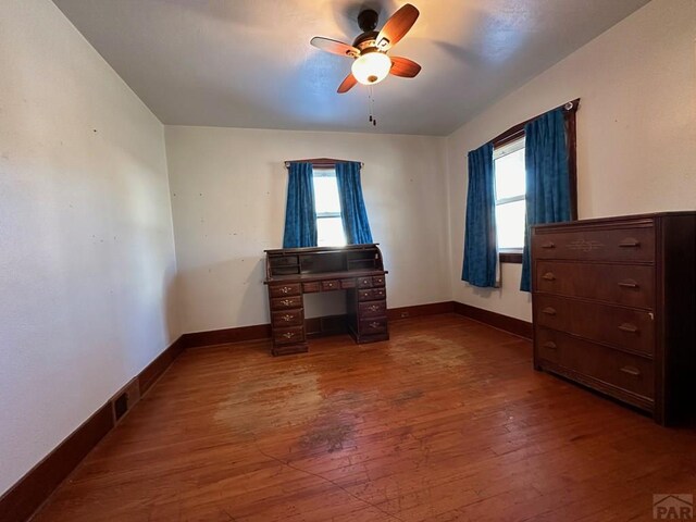 unfurnished bedroom featuring multiple windows, dark wood finished floors, and baseboards