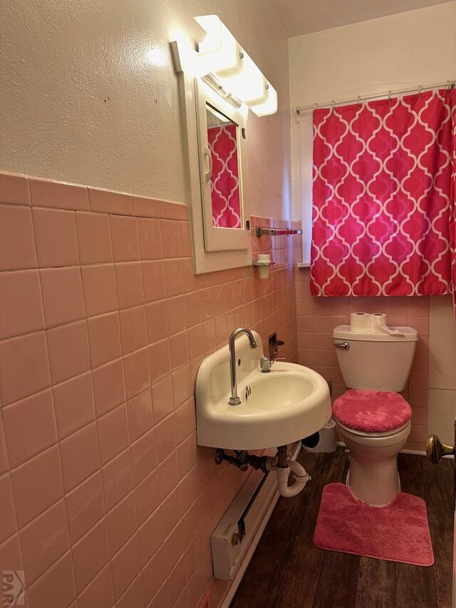 bathroom with tile walls, wainscoting, toilet, wood finished floors, and a sink